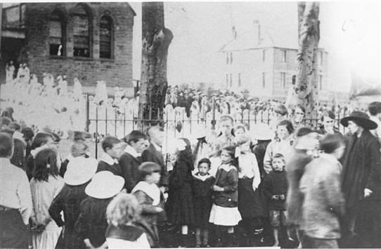 Photo:The May Procession gathers in front of the Catholic School.  In the background the Chapel House, but as yet no Chapel. This dates the photo to the early 1920s..